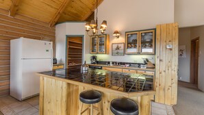 A kitchen with a central island, wooden bar stools, a refrigerator, and a wooden ceiling. - Wrap Around Deck | Unmatched Views | Air Conditioning | STR2025-060 (Ridgway)