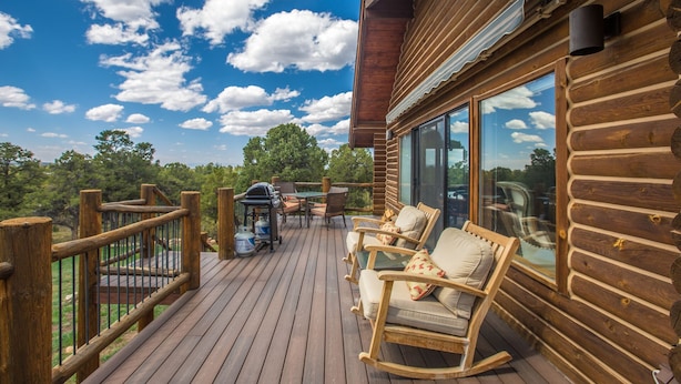 A wooden deck with outdoor furniture and a grill, overlooking a forested area. - Wrap Around Deck | Unmatched Views | Air Conditioning | STR2025-060 (Ridgway)