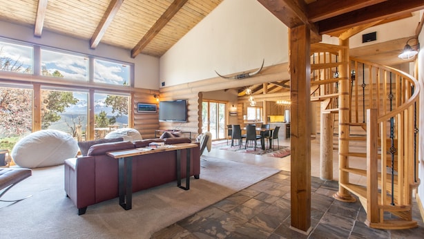 A spacious living area with a fireplace, a large window overlooking a scenic view, and a wooden staircase.
