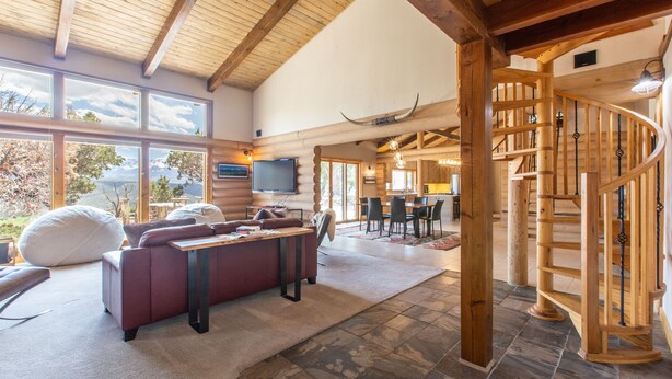 A spacious living area with a fireplace, a large window overlooking a scenic view, and a wooden staircase. - Stunning Views | Spacious | Trail Access | Air Conditioning STR2025-060 (Ridgway)