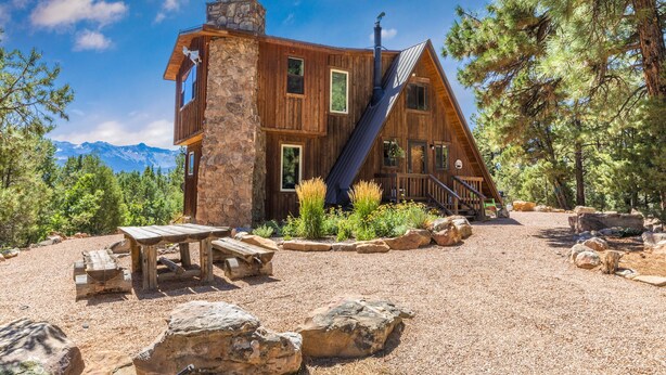 A rustic cabin with a stone chimney, wooden exterior, and a gravel driveway.