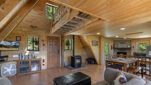 A cozy cabin interior with a fireplace, wooden furniture, and a dining area.