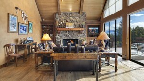 A spacious living room with a stone fireplace, wooden ceiling, and large windows offering a mountain view. - Mountain Retreat | Stunning Views | A/C | Hot Tub STR2025-062 (Ridgway)
