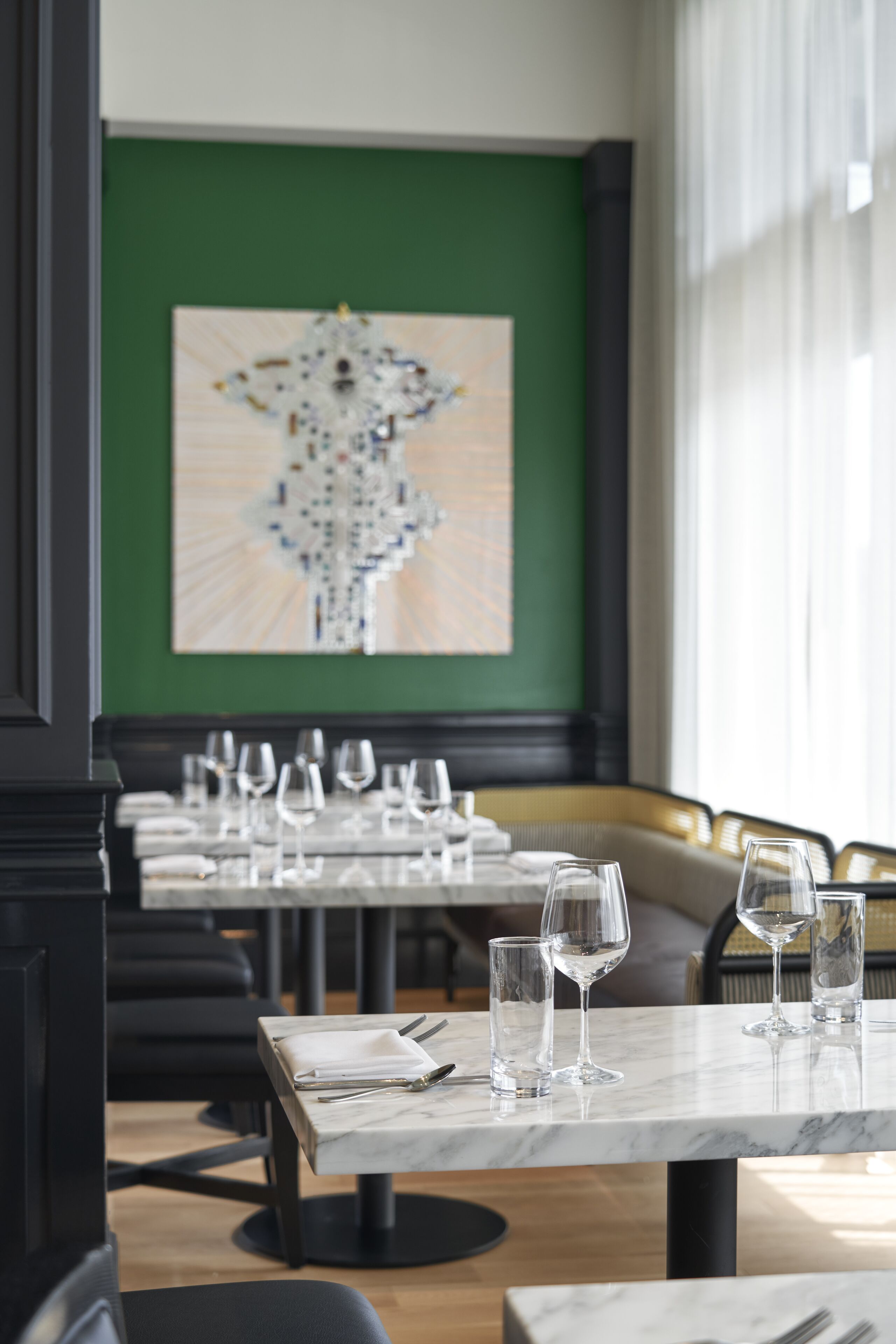 A restaurant with marble tables, green walls, and a large abstract painting.