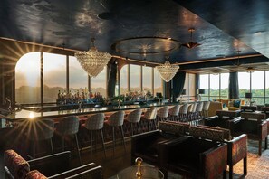 A bar area with a long counter, multiple bar stools, and a seating area with sofas and chairs.