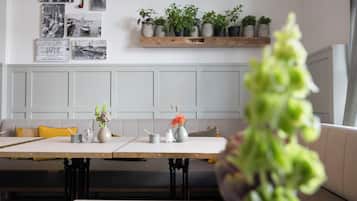 Un comedor con una mesa larga, sillas, un banco y una pared decorada con cuadros y plantas en macetas.
