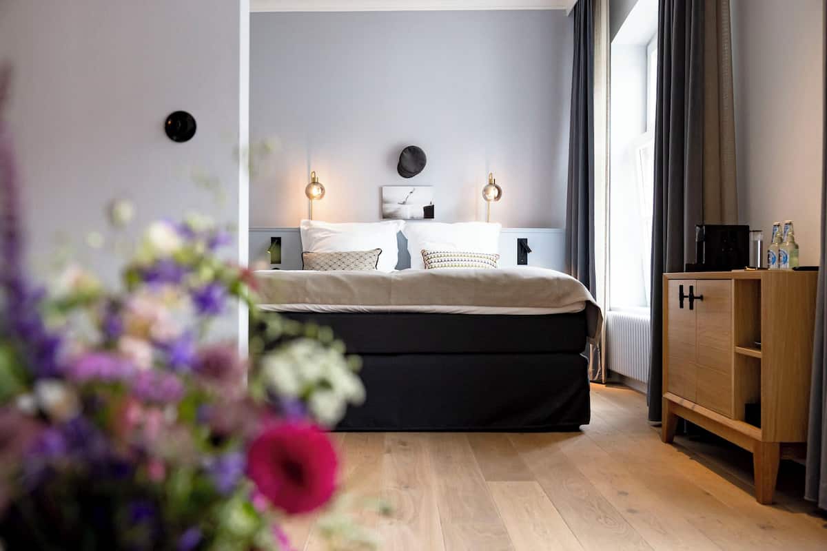 Een slaapkamer met een bed, nachtlampjes, een houten kast en een raam met gordijnen.