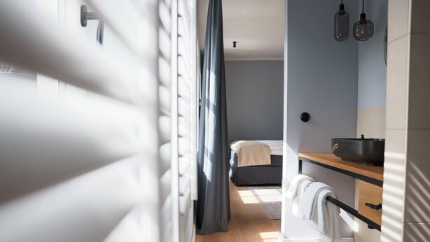 A modern bedroom with a bed, a bedside table, and a window with curtains. - Boutiquehotel Petuh am Hafen - adults only (Flensburg)