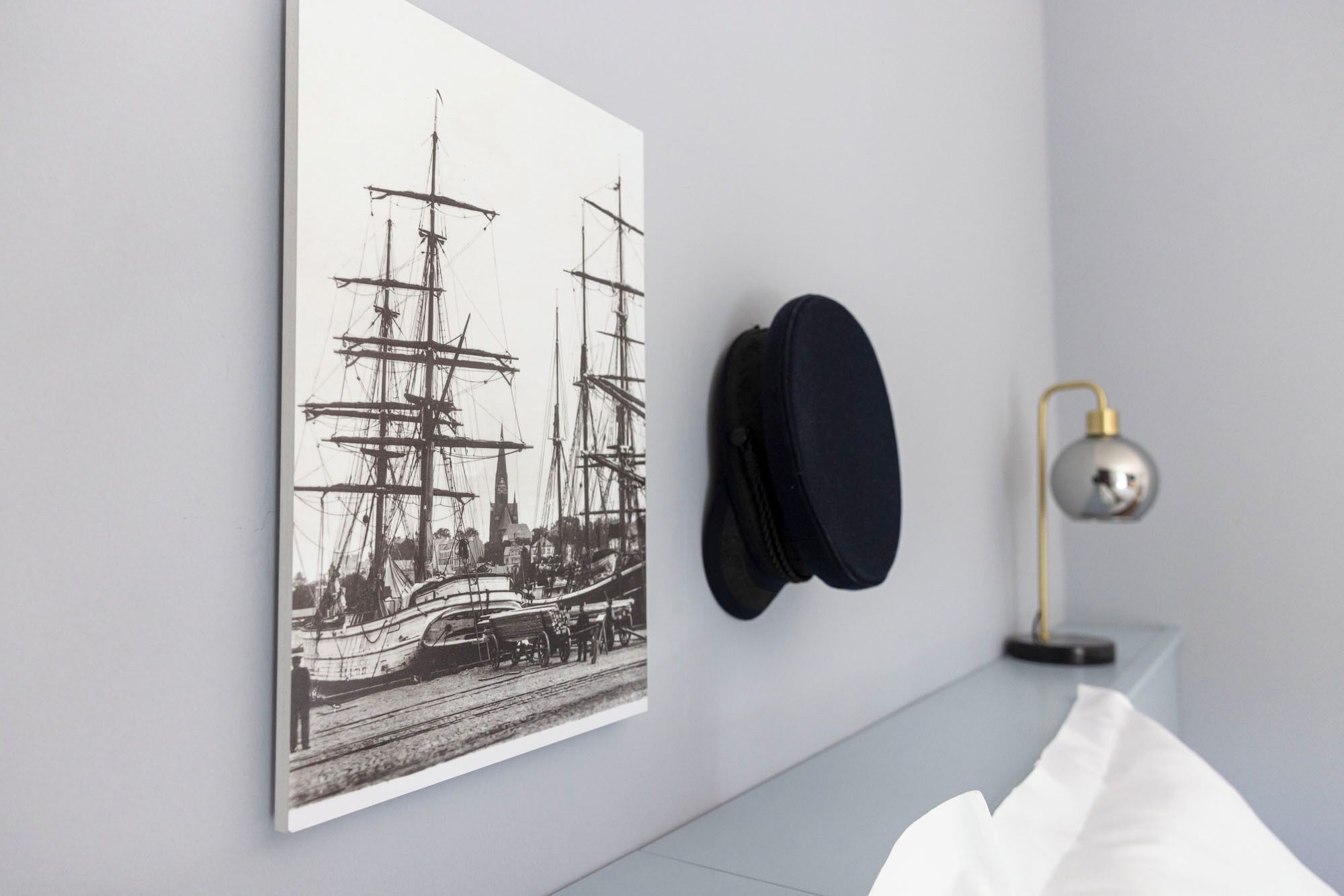 Eine Wand mit einem maritimen Kunstwerk, einem Hut und einer Lampe.