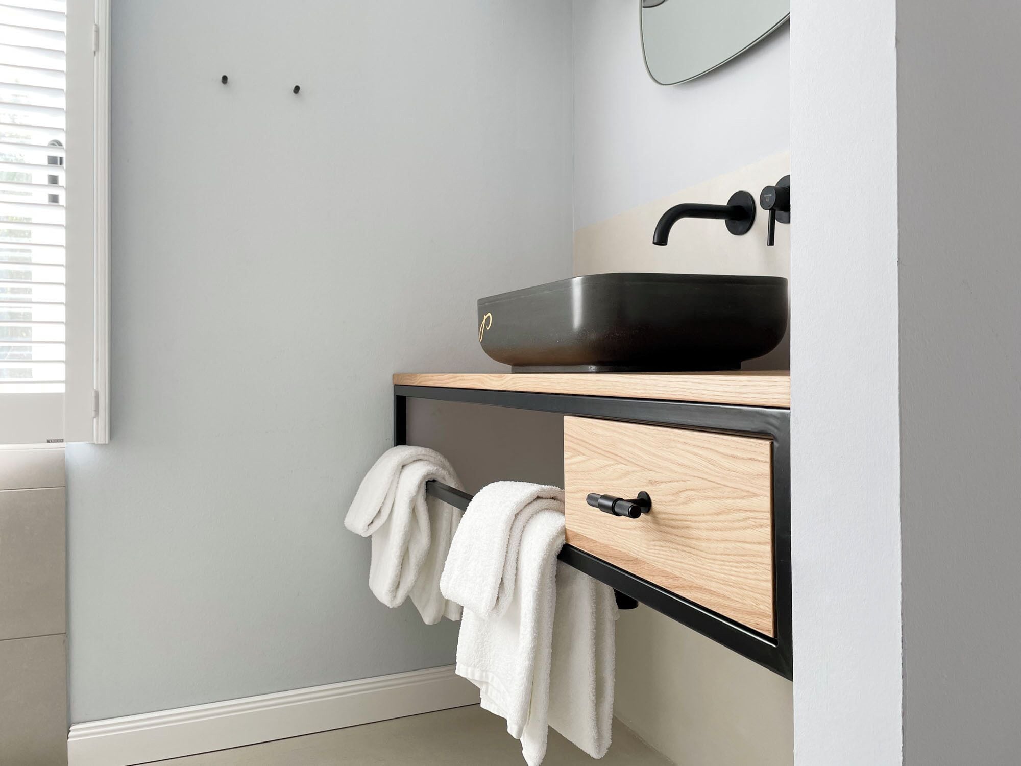Une salle de bain avec un lavabo noir, un meuble-lavabo en bois et un porte-serviettes.