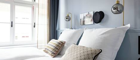 A bedroom with a bed, pillows, a wall-mounted lamp, and a window with curtains.