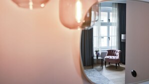 A room with a large mirror reflecting a pink chair, a small table with a vase, and a window with curtains. - Boutiquehotel Petuh am Hafen - adults only (Flensburg)