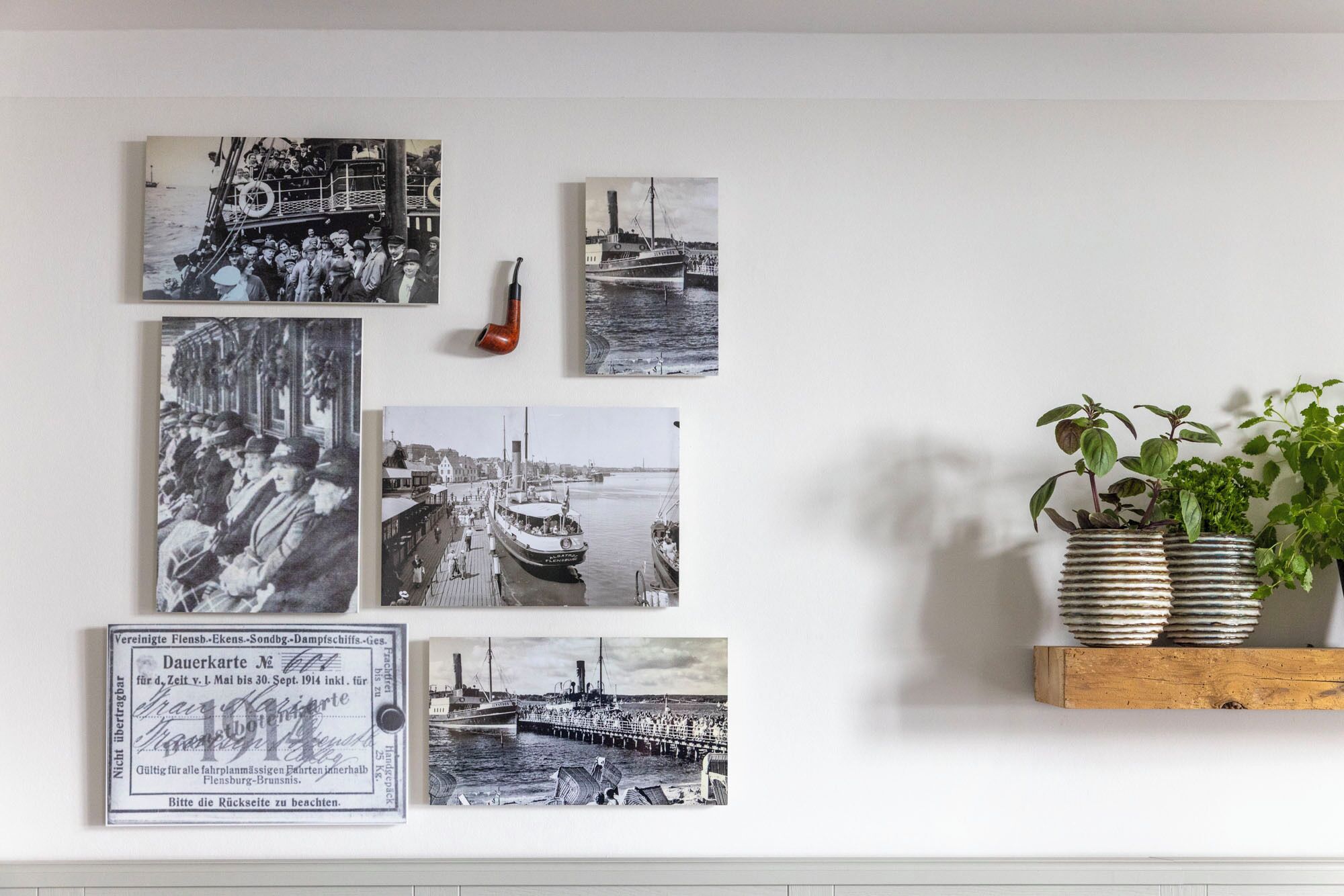 Eine Wand mit Schwarz-Weiß-Fotos von Booten und einem alten Fahrkartenstempel.