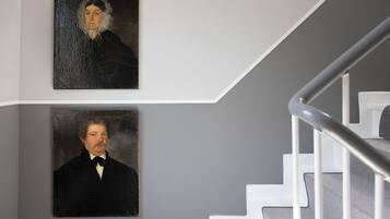 Two portraits on a wall, a staircase with white railings, and a grey wall.