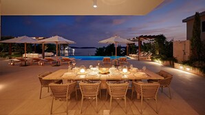 An outdoor dining area with a view of the sea, equipped with umbrellas and lounge chairs.