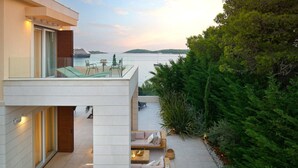Une terrasse extérieure moderne, dotée d’un espace salon, d’une balustrade en verre et offrant une vue sur la mer.