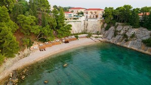Un hôtel situé sur la côte, avec une plage, des chaises longues et une falaise rocheuse.