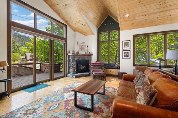 A spacious living room with a fireplace, large windows, a wooden ceiling, and a cozy seating area.