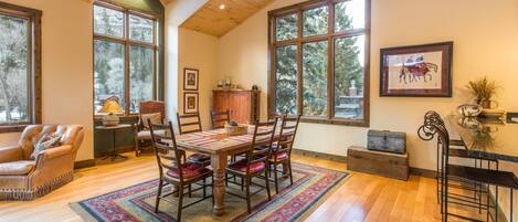 A spacious room with a wooden ceiling, large windows, a dining table with chairs, a fireplace, and a bar area.
