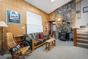 A cozy living room with a stone fireplace, wooden furniture, and a framed poster on the wall.