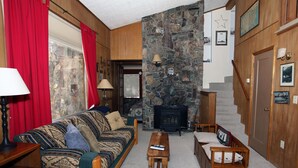 Una sala de estar acogedora con chimenea de piedra, muebles de madera y una cortina roja.