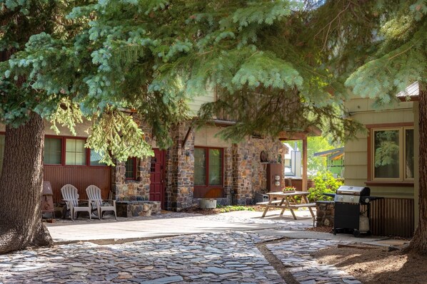 A stone patio with outdoor seating, a barbecue grill, and a stone building with a red door.