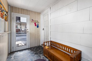 A hallway with a wooden bench, a door with a window, and a wall with a pegboard holding items.