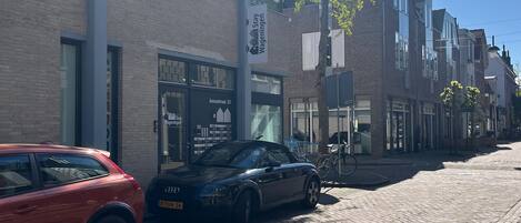 A street scene with parked cars, a building with a sign reading "Stay Stay Wageningen," and a clear blue sky.