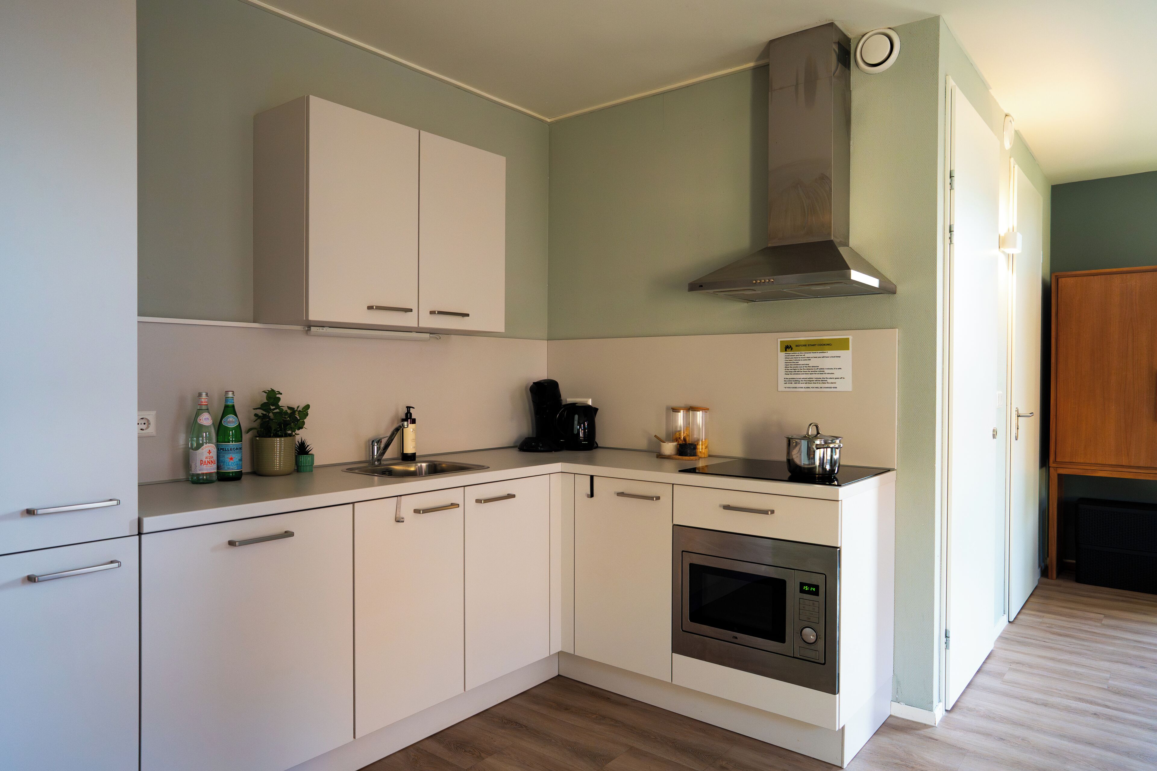 A modern kitchen with white cabinets, a stainless steel oven, a coffee maker, and a range hood.