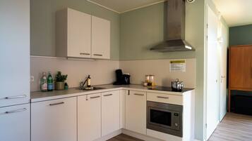 A modern kitchen with white cabinets, a stainless steel oven, a coffee maker, and a range hood.