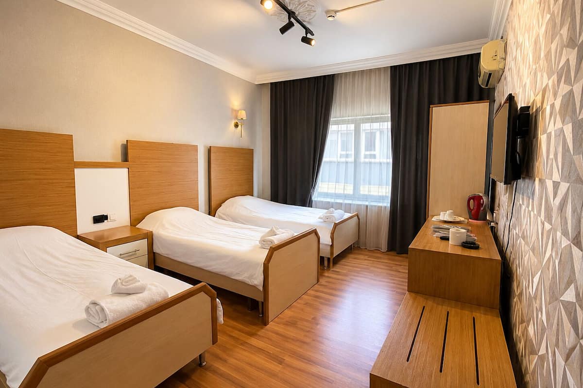 A hotel room with two beds, a desk, a chair, a TV, and a window with curtains.