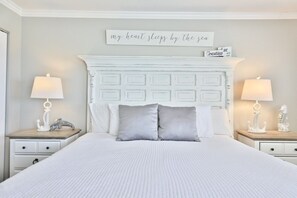 Une chambre à coucher bien aménagée, avec un grand lit, deux tables de chevet avec des lampes, une tête de lit blanche et un panneau décoratif au-dessus du lit.