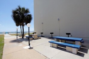 Un espace extérieur aménagé avec des bancs et des tables, un palmier et un bâtiment blanc offrant une vue sur la plage.
