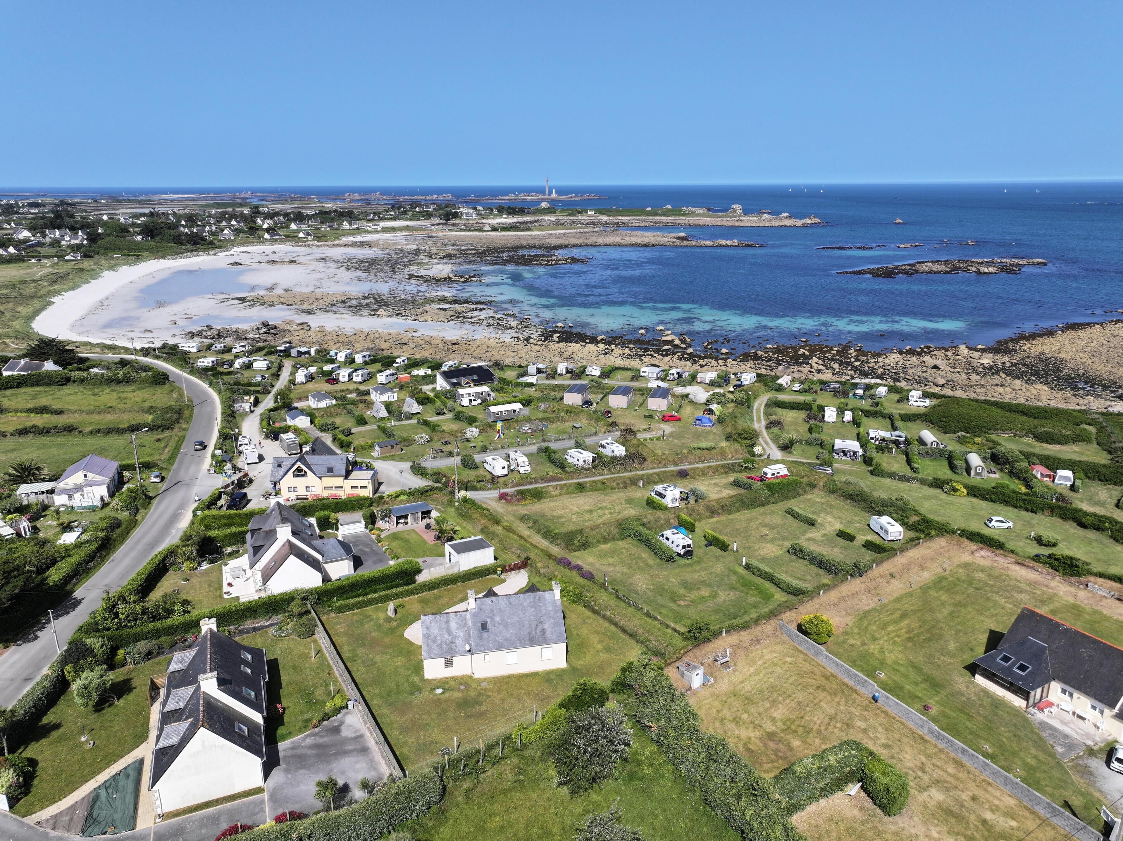 An aerial view of a coastal area with a mix of residential houses and RVs, a winding road, and a beach.