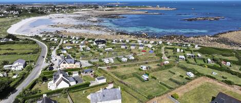 An aerial view of a coastal area with a mix of residential houses and RVs, a winding road, and a beach.