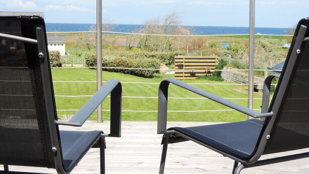 Two black chairs on a wooden deck with a view of a grassy area and a wooden fence. - 4-star villa, 230 m², heated pool, steam room, ocean view, beach 200 m away—sleeps 8. (Plouguerneau)