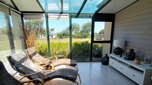 A modern living room with two lounge chairs, a white cabinet with decorative items, and a view of a garden through large glass windows. - 4-star villa, 230 m², heated pool, steam room, ocean view, beach 200 m away—sleeps 8. (Plouguerneau)
