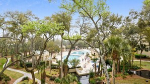 Een resort met een zwembad, omringd door palmbomen en een helderblauwe lucht.