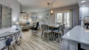 A modern kitchen with a central island, a dining area with wooden chairs, and a living space with a sofa and lamps. - 174 Colonnade Club - Shipyard - 2 Bed 2 Bath Sleeps 5 - Hilton Head Rentals (Hilton Head Island)