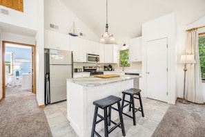 A modern kitchen with white cabinetry, a central island with stools, a microwave, and a sink. - Do Duck Inn 4 Bedroom Home in the Heart of Duck (Duck)
