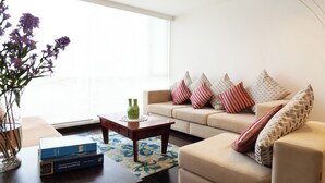 A living room with a sofa, a coffee table, a vase with flowers, and a bookshelf. - 3BR La Carolina Quito Parking Sleeps 8 Galapagos Base 700Mbps (Quito)