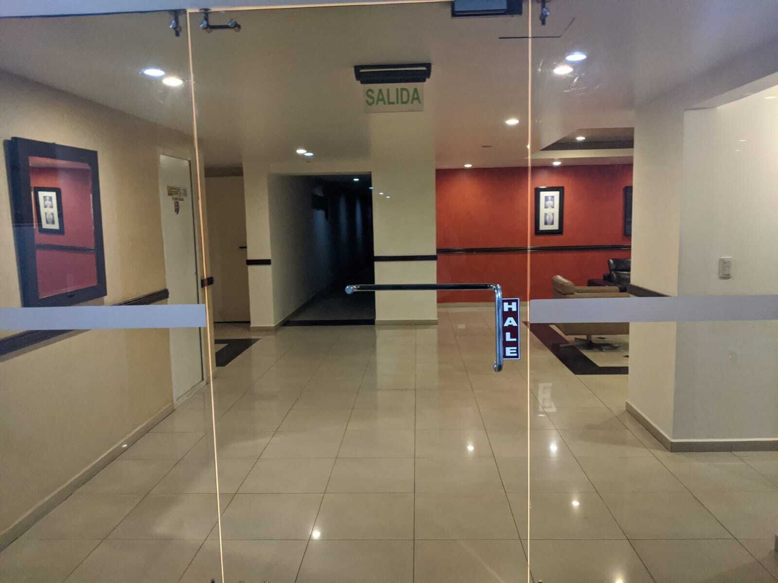 Un vestíbulo de hotel con un panel de vidrio, un letrero que dice "SALIDA" (salida) y un letrero "HALE" que indica una zona para fumadores.