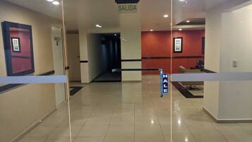 Un vestíbulo de hotel con un panel de vidrio, un letrero que dice "SALIDA" (salida) y un letrero "HALE" que indica una zona para fumadores.