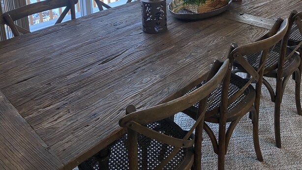 Uma área de refeições com mesa e cadeiras de madeira, uma planta em vaso e vista para um deck coberto de neve através de grandes janelas.