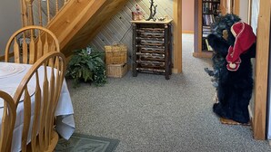 Um quarto acolhedor com uma escada de madeira, uma mesa de jantar com cadeiras, uma mesinha com abajur e uma estante de livros.
