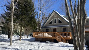 Uma casa com deck de madeira e fachada de pedra, rodeada por neve e árvores.