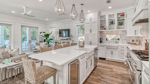 A spacious kitchen with white cabinetry, a large island, and a dining area with wicker furniture. - Exquisite Retreat: Enjoy Luxurious Comfort with a Private Pool, Spa, Bikes, and More! (Santa Rosa Beach)