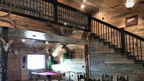 Un interior de madera con mesa de billar, zona de comedor y una escalera.