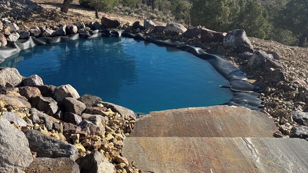 Una piscina natural rodeada de rocas y árboles, con vistas a montañas distantes.