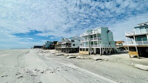 Una propiedad frente a la playa con varias edificaciones sobre pilotes, una playa arenosa y un cielo despejado.